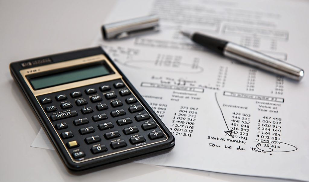 A calculator, pen and accounting sheet on table